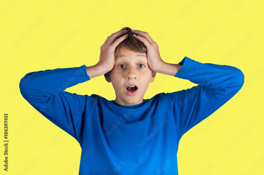 astonished boy in blue pullover holding his hands on head. Emotional portrait of caucasian teen boy. astonished boy in blue pullover holding his hands on head. Emotional portrait of caucasian teen boy.
