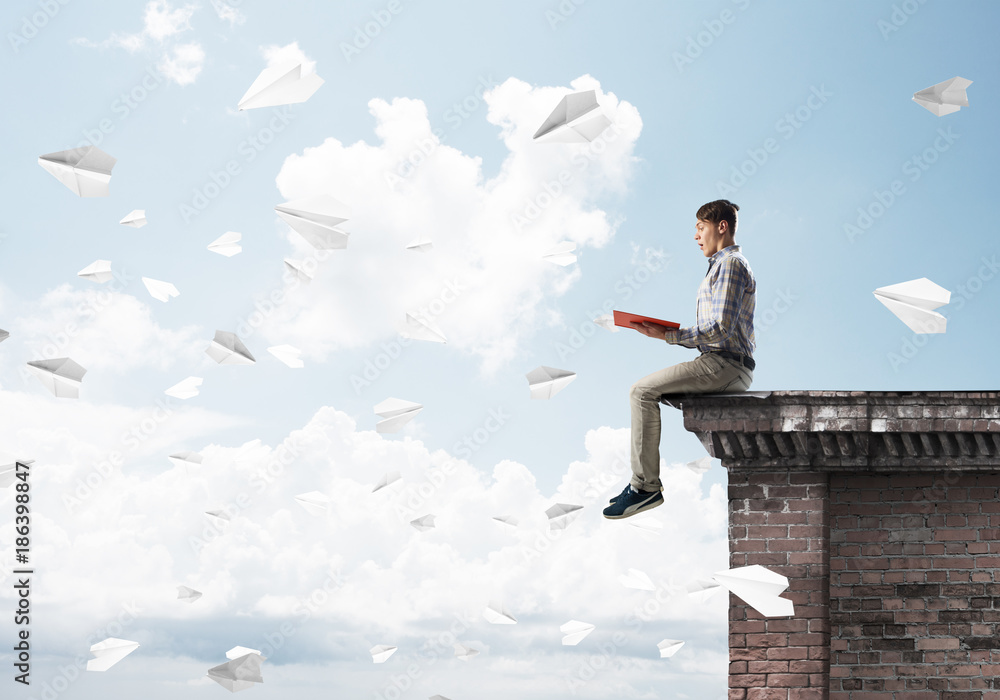 Handsome student guy on roof edge reading book and paper planes fly around Handsome student guy on roof edge reading book and paper planes fly around
