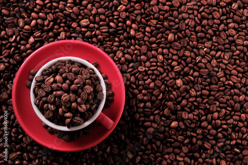 Red coffee cup and saucer one single for espresso or capuccino on a background of scattered dark coffee beans photo