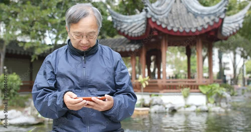 Asian senior man watching on cellphone in chinese garden Asian senior man watching on cellphone in chinese garden