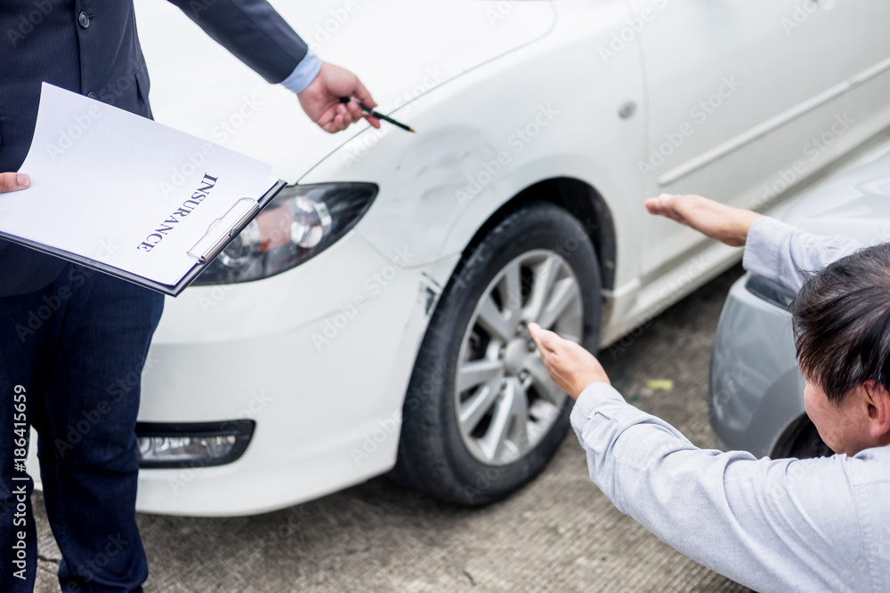Insurance agent writing on clipboard while examining car after accident claim being assessed and processed. Insurance agent writing on clipboard while examining car after accident claim being assessed and processed.