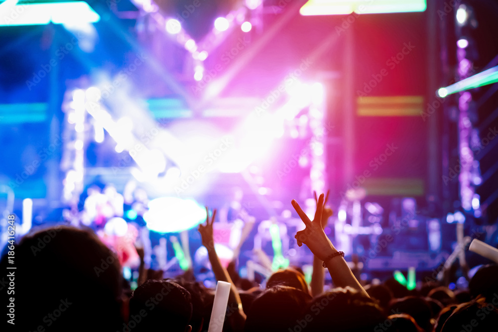 Hand gesture victory finger at concert stage lights crowd or audience artist band in the music festival rear view with spotlights glowing effect and people fan audience silhouette raising hands up