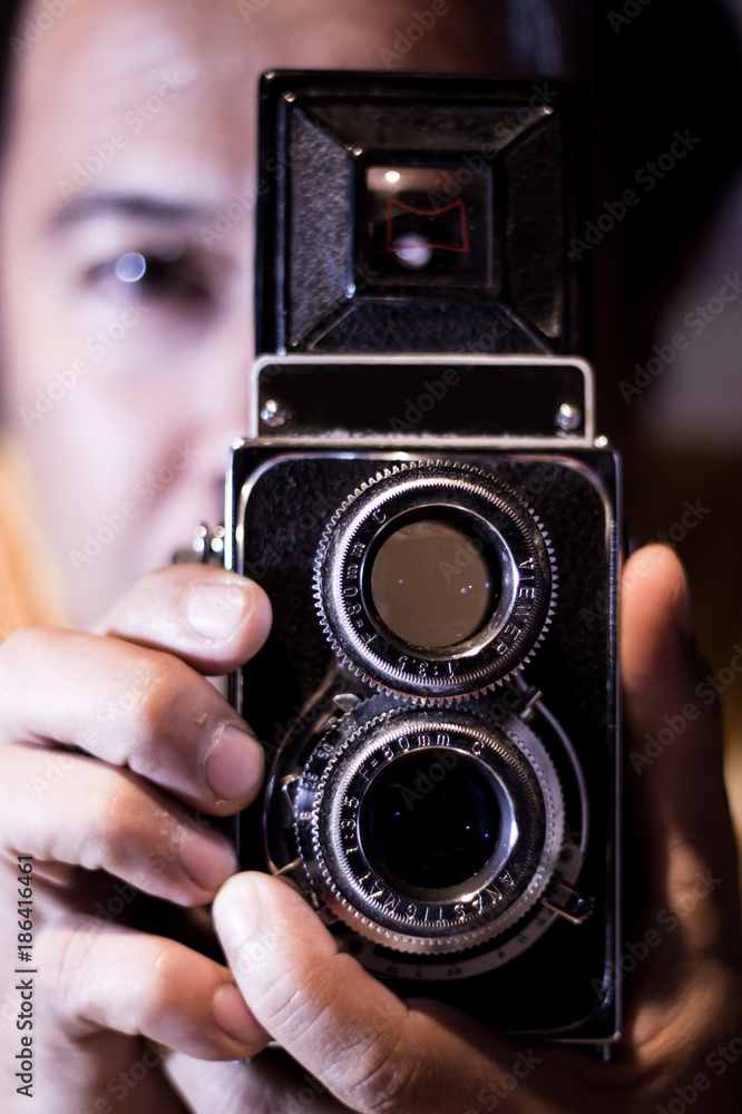 Man with old vintage camera in hands. Focus to man eyes. Vintage stylized photo of man photographer with old TLR (Twin Lens Reflex) Camera, ring-flash shot..