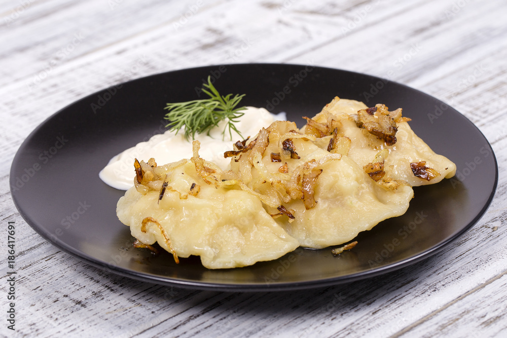 Ukrainian and Russian dishes - vareniki or dumplings with mashed potatoes or cottage cheese, fried onions and sour cream on wooden background