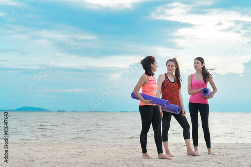 Asian women yoga teenager together talking on the beach with yoga mat at seaside after practice exercise healthy lifestyle sporty, Copy space the left.