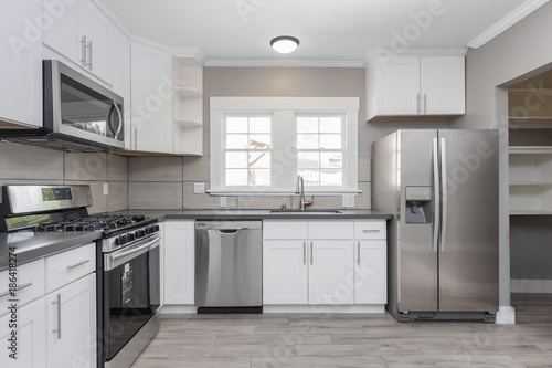 Kitchens in white new, with granite counter-tops, stove and stainless steel refrigerator.