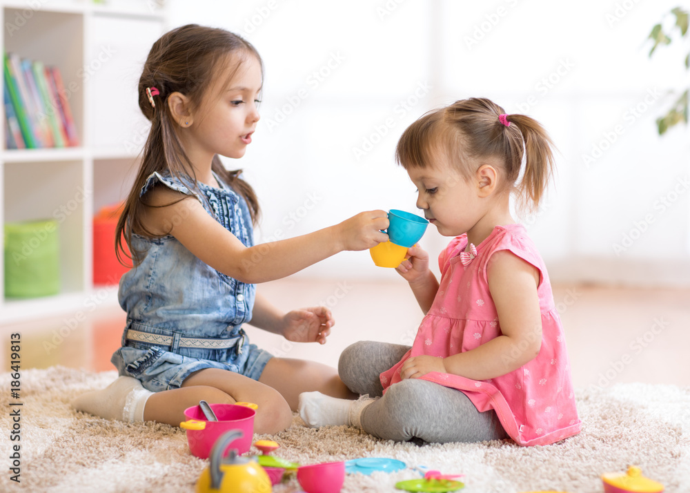 Little happy children, cute toddler and kid girls play with plastic toy kitchen on floor at home or kindergarten Little happy children, cute toddler and kid girls play with plastic toy kitchen on floor at home or kindergarten