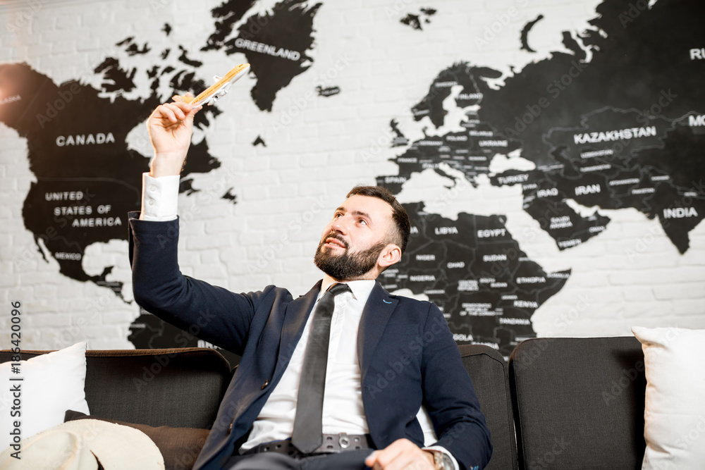 Handsome male agent playing with toy airplane at the travel agency office with world map on the background Handsome male agent playing with toy airplane at the travel agency office with world map on the background
