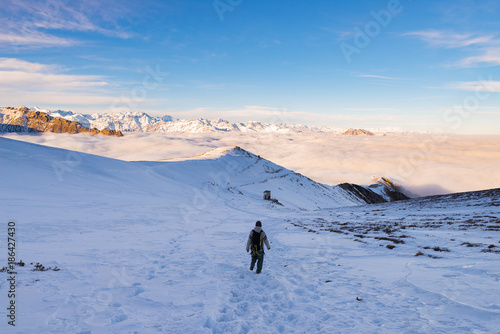 Backpacker hiking on snow on the Alps. Rear view, winter lifestyle, cold feeling, majestic mountain landscape.
