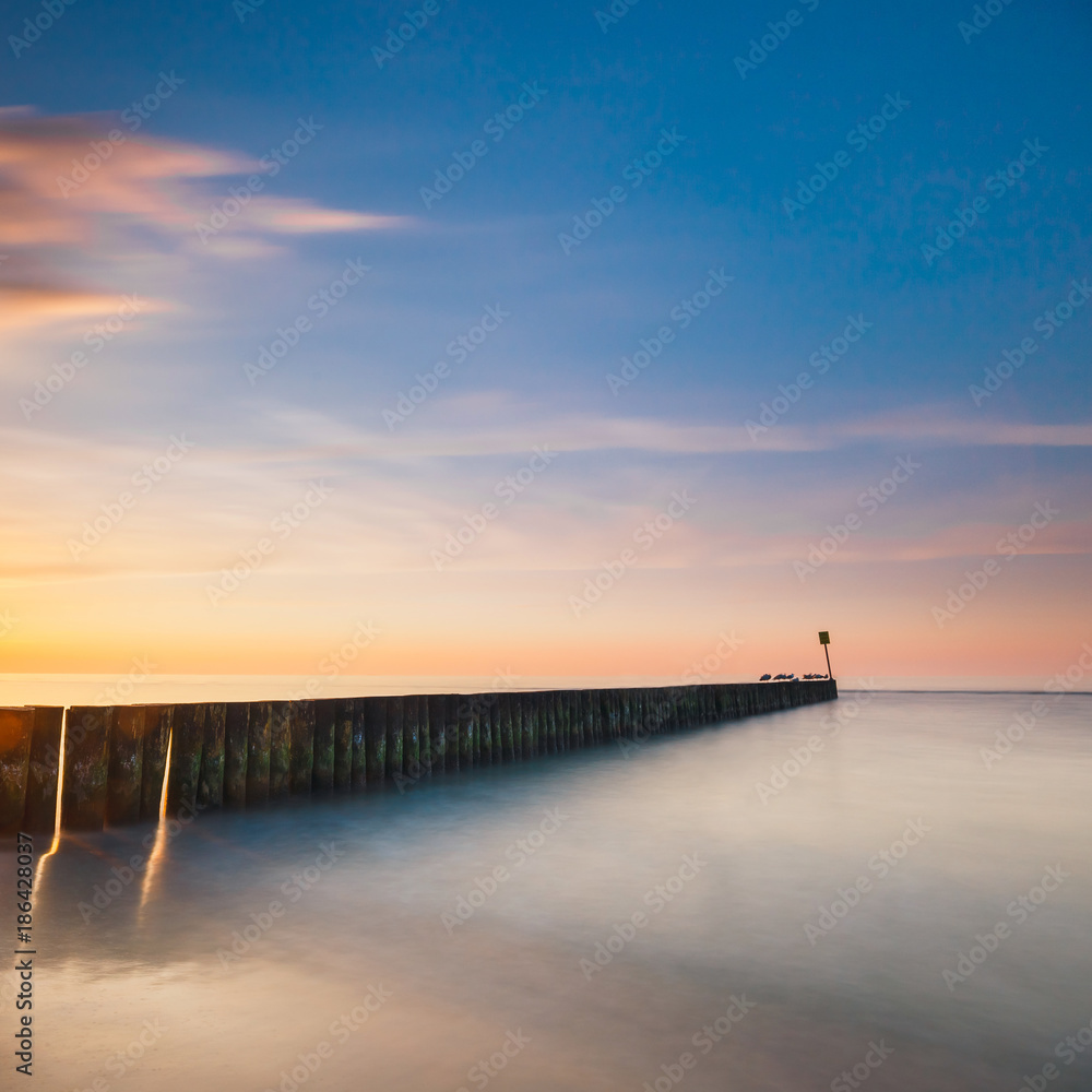 Sunset on the beach with a wooden breakwater, long exposure