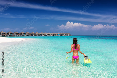 Frau im Bikini und mit Schnorchelausrüstung steht am tropischen Strand der Malediven