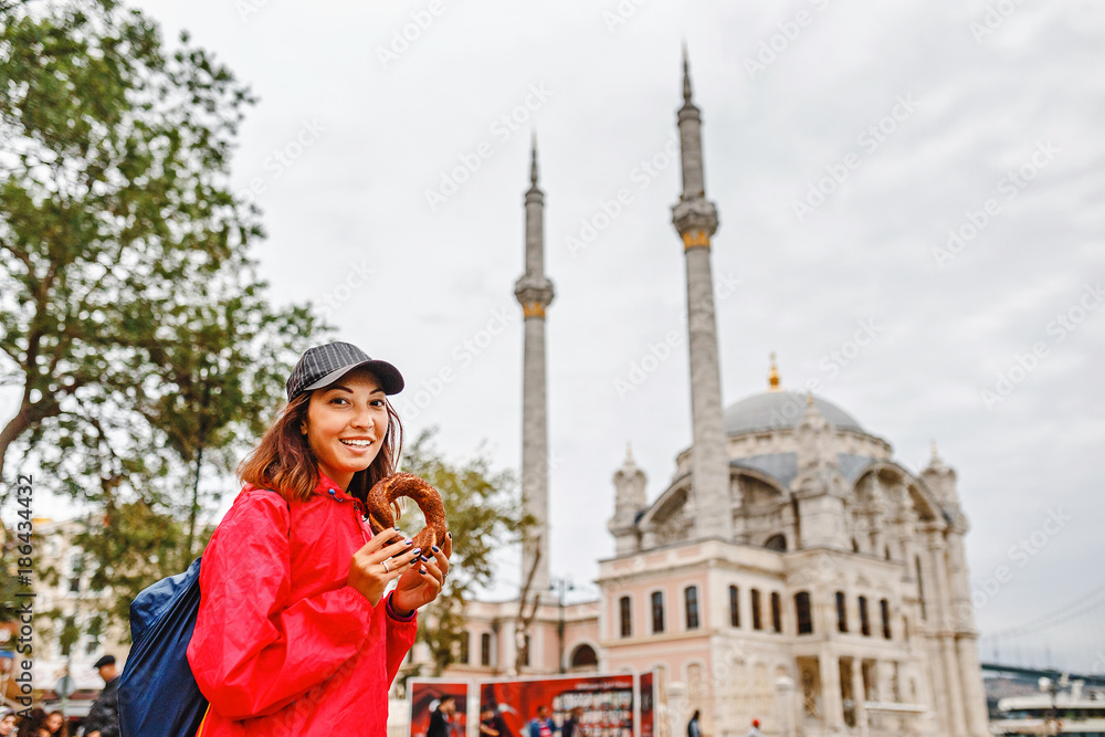 Young woman eating turkish bagel in Istanbul, Turkey on the background of Ortakoy mosque