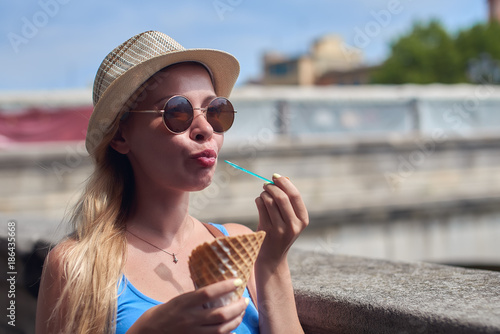 Young blondie  woman with sunglasses enjoying ice cream cone on a river embankment.