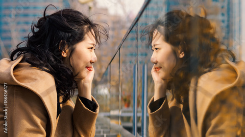 Beautiful Chinese girl looking at her mirror image in glass. photo
