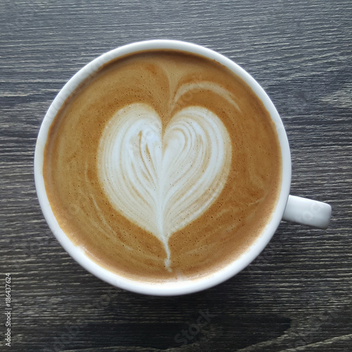 Top view of a mug of latte art coffee on timber background.