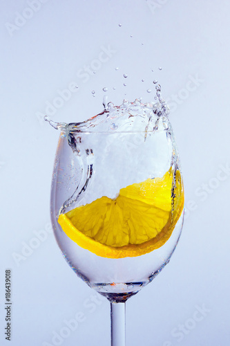 A slice of lemon falls into the glass with vodka. Bubbles and splashes appear