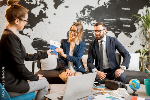 Young businesscouple choosing a trip with agent sitting at the travel agency office with world map on the background photo