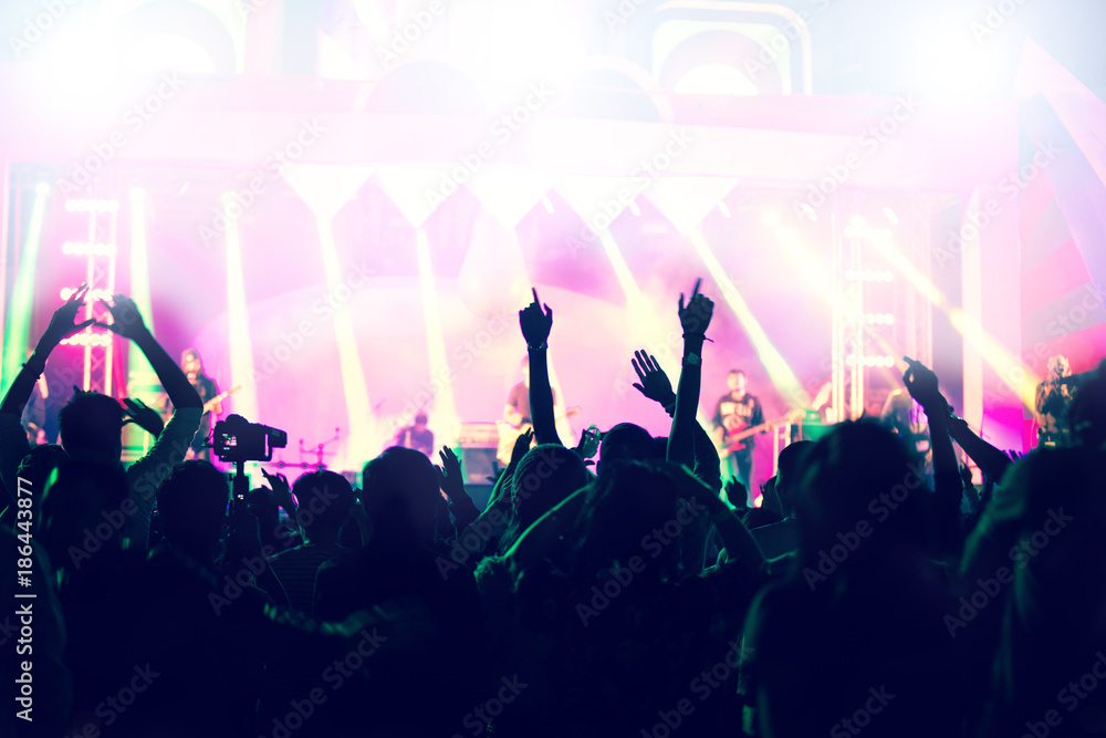 silhouettes of concert crowd at Rear view of festival crowd raising their hands on bright stage lights