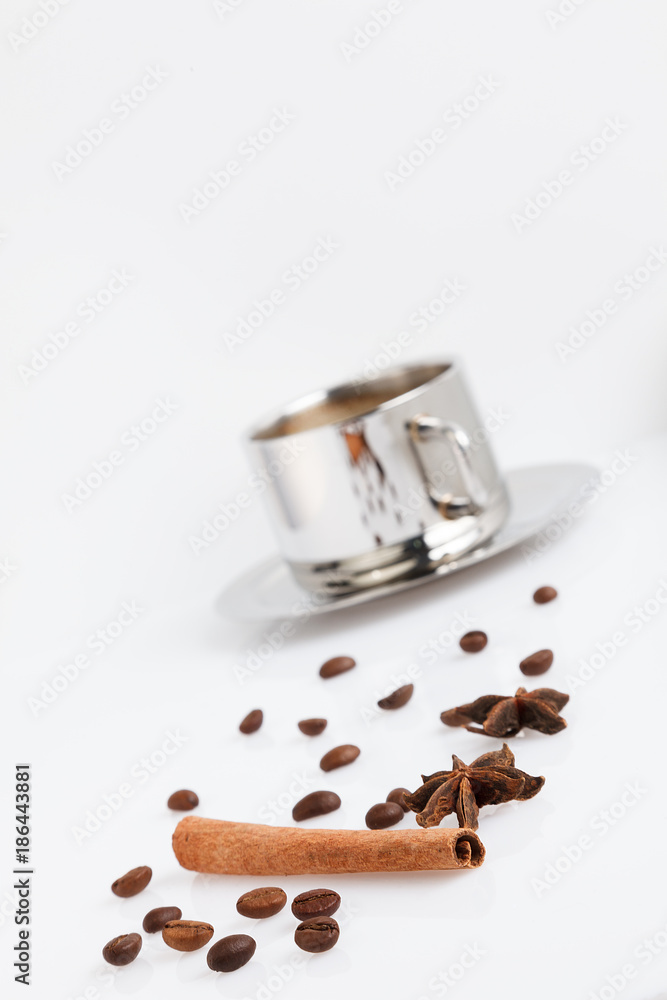 Grains of coffee with cinnamon and anise on white table. There is a cup of coffee behind. Grains of coffee with cinnamon and anise on white table. There is a cup of coffee behind.