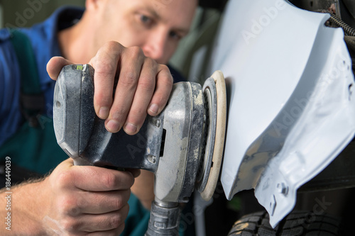 Grinder in the hands of a man who sharpen a car varnish in the car shop.