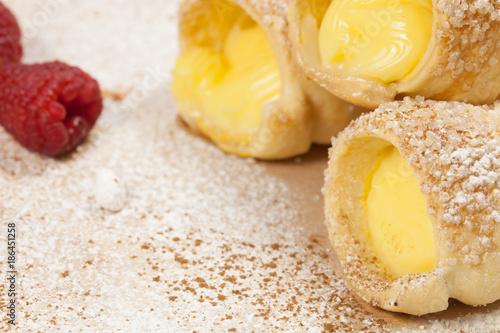 Puff pastry vanilla custard horns and raspberries on a wooden board