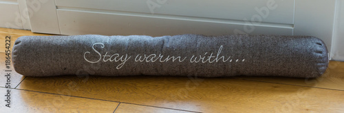 A roll with letters keeping warm inside the house by protecting from air draft and saving heating costs in the winter time. draught exluder against the cold winter outside.