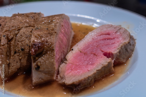 roasted pork fillet with a wine and balsamico sauce, arranged on a white plate. The medium cooked meat is cut into delicious slices.