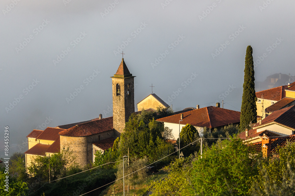 View down to a village in the tuscany in italy. Village is lying in the mist, only the church and small house can be seen.