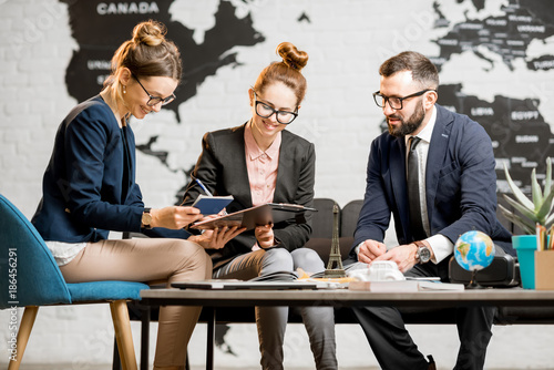Young businesscouple choosing a trip with agent sitting at the travel agency office with world map on the background