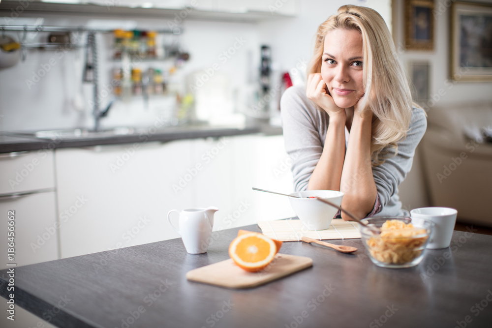 Beautiful blond caucasian woman posing in her kitchen, while drinking coffee or tea and eating a healthy breakfast meal full of cereal and other healthy foods, including fruit Beautiful blond caucasian woman posing in her kitchen, while drinking coffee or tea and eating a healthy breakfast meal full of cereal and other healthy foods, including fruit