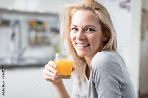 Beautiful blond caucasian woman posing in her kitchen, while drinking coffee or tea and eating a healthy breakfast meal full of cereal and other healthy foods, including fruit