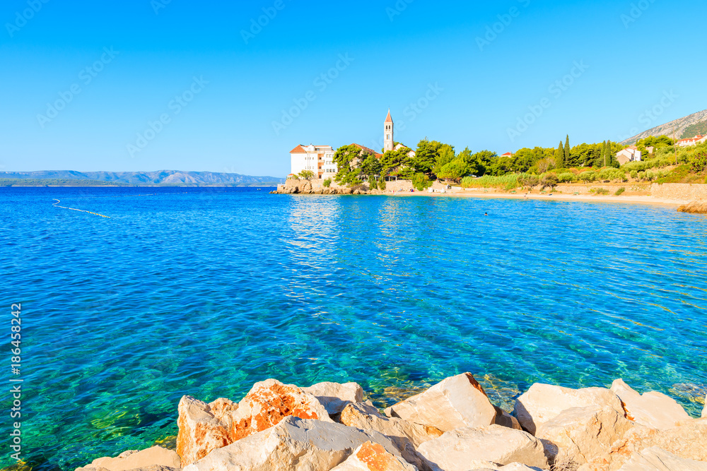 Fototapeta premium Rocks and beautiful sea water with Dominican monastery in distance, Bol town, Brac island, Croatia