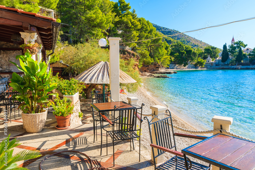 Tables with chairs of small coastal restaurant on beach in Bol town, Brac island, Croatia