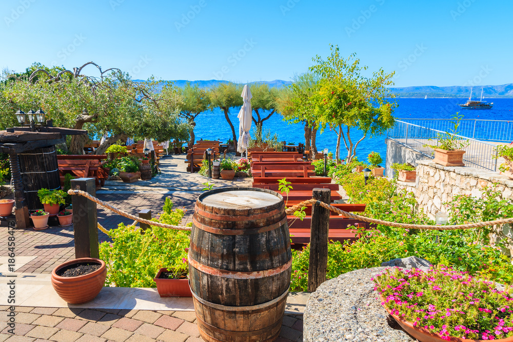 Fototapeta premium BOL TOWN, BRAC ISLAND - SEP 14, 2017: Traditional restaurant decorated with flowers and wine barrels with sea view in Bol town, Brac island, Croatia.