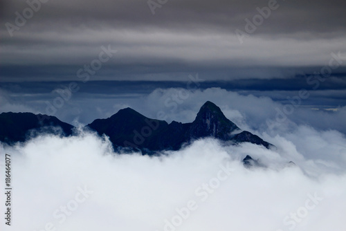 Sharp peaks of Carnic Alps main ridge rise above low level clouds in overcast summer evening, Cima Avostanis Blaustein, Creta di Timau Hocheck, Friuli Venezia Giulia Italy / Carinthia Austria Europe