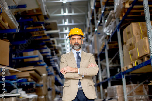 Portrait of senior businessman in suit with helmet in a warehouse