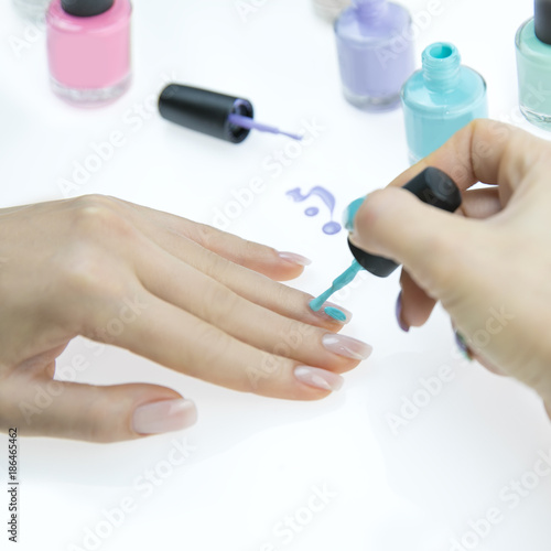 Close up of woman hands with nail polishes of different colors. Woman applying nail polish on her nail carefully.