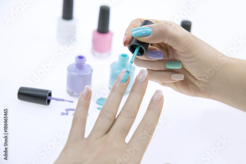 Close up of woman hands with nail polishes of different colors. Woman applying nail polish on her nail carefully.