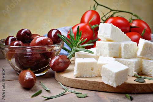 Feta cheese with kalamata olives, tomatoes and rosemary on wooden background