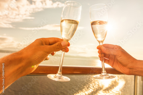 Luxury cruise ship travel couple toasting champagne glasses for celebration honeymoon. Caribbean holiday drinking doing cheers at sunset view sun flare of cruise holiday destination.
