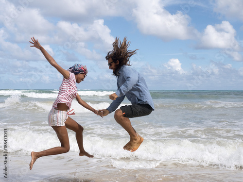 A girl and a man are jumping near the sea