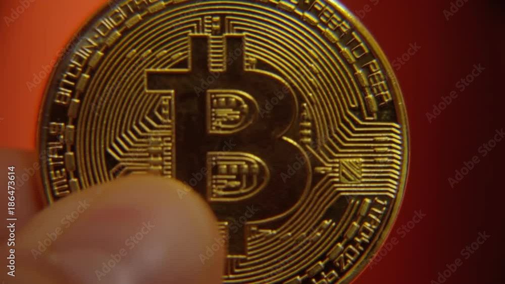A hand lifting a physical golden bitcoin (digital virtual crypto-currency) until it comes in focus. Clear extreme close-up shot.
