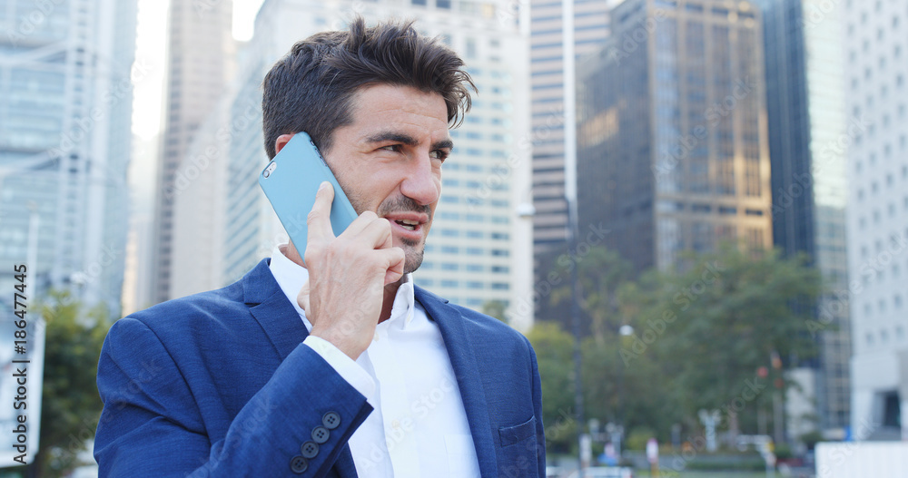 Businessman talk to cellphone over cityscape background, serious talking, replying customer Businessman talk to cellphone over cityscape background, serious talking, replying customer
