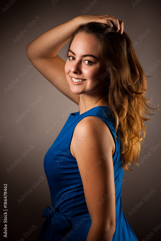 Fototapeta premium Portrait of beautiful young caucasian woman in blue dress over dark gray background
