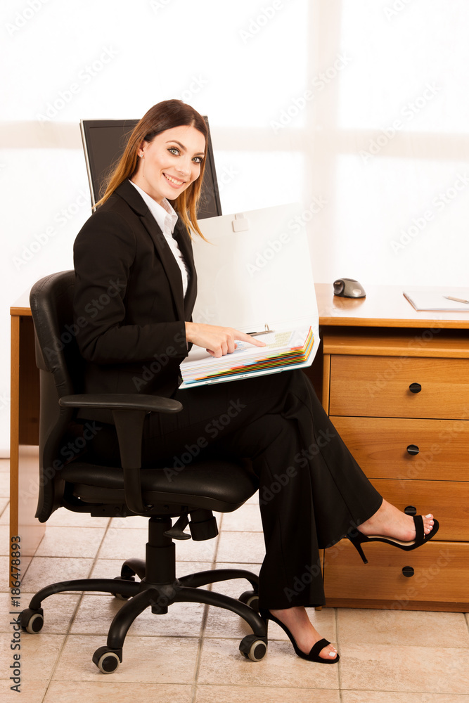 Young business woman with bold folder checking data at her desk in the office Young business woman with bold folder checking data at her desk in the office