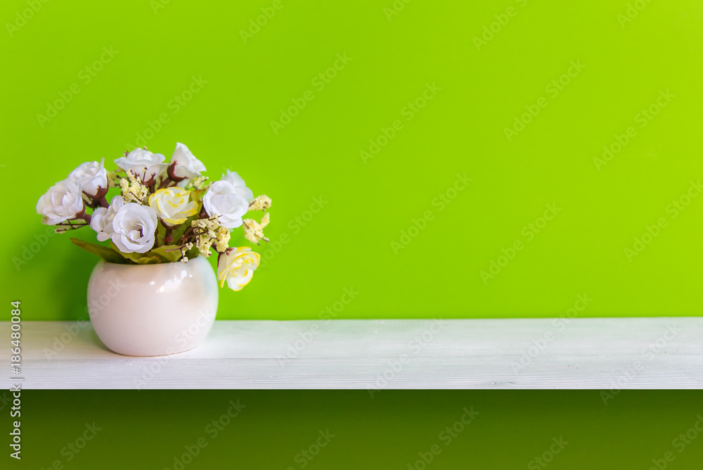 Green wall with flowers on shelf white wood, copy space for test. Still life Concept