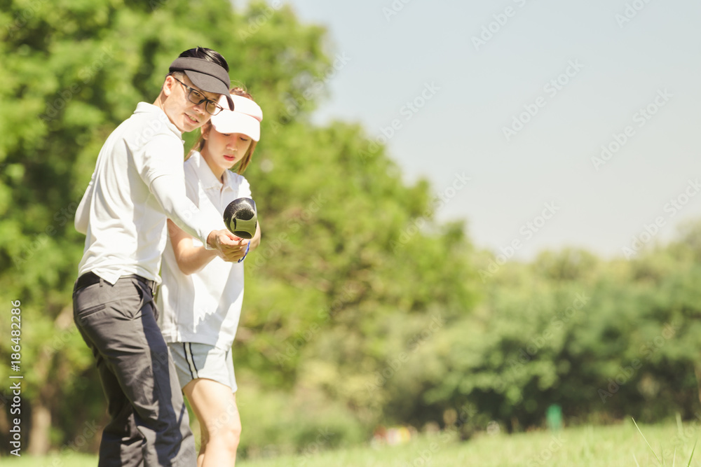 Naklejka premium Asian couple playing golf. man teaching woman to play golf while standing on field