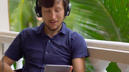 man in tropics talking with friends and family on video call using a tablet and wireless headphones photo