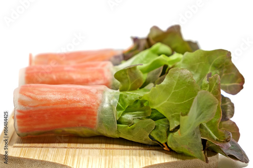 Salad roll in noodle with carrot and fresh vegetables on wooden plate and white background, heathy eating concept