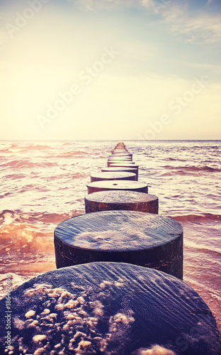 Vintage toned close up picture of an old wooden groyne on a beach at sunset, peaceful natural background, selective focus.